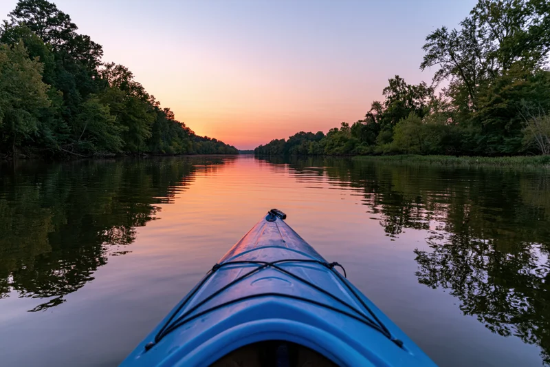 Blue kayak bow pointing forward on calm river at sunset surrounded by forest