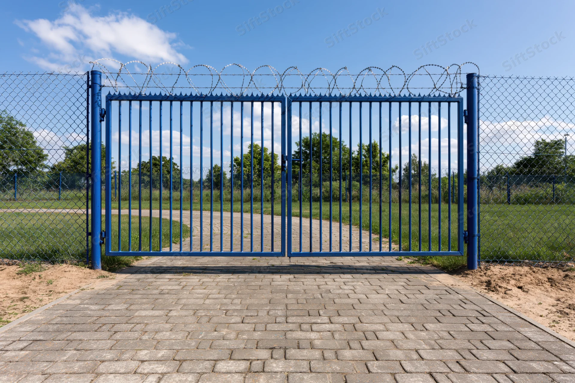 Blue steel security gate with vertical bars and razor wire on chainlink fence at outdoor entrance
