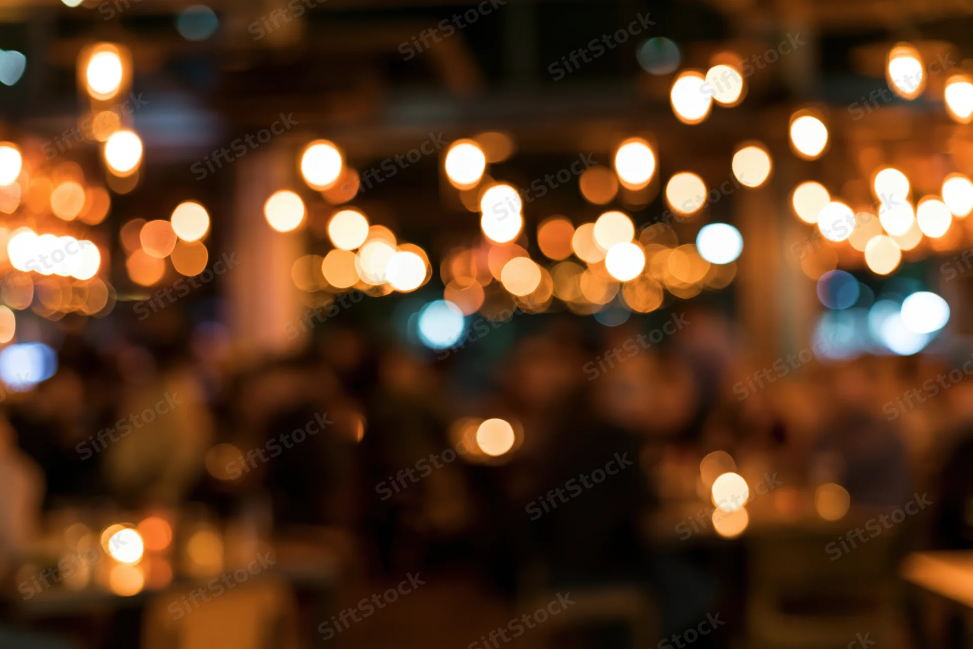 Blurred view of people dining at tables in a dimly lit restaurant interior with warm glowing lights