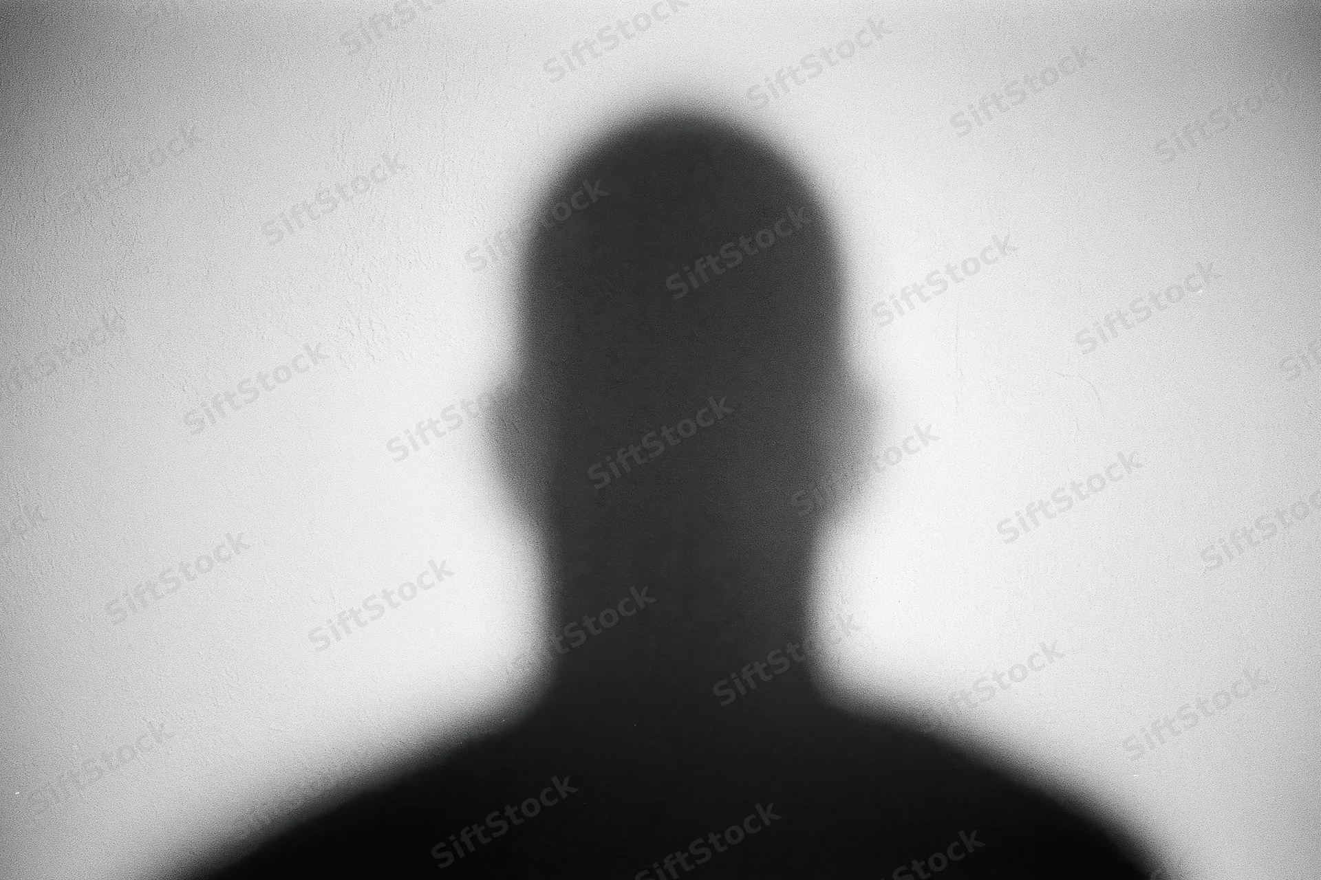 Blurred silhouette of a person's head and shoulders cast on a white wall