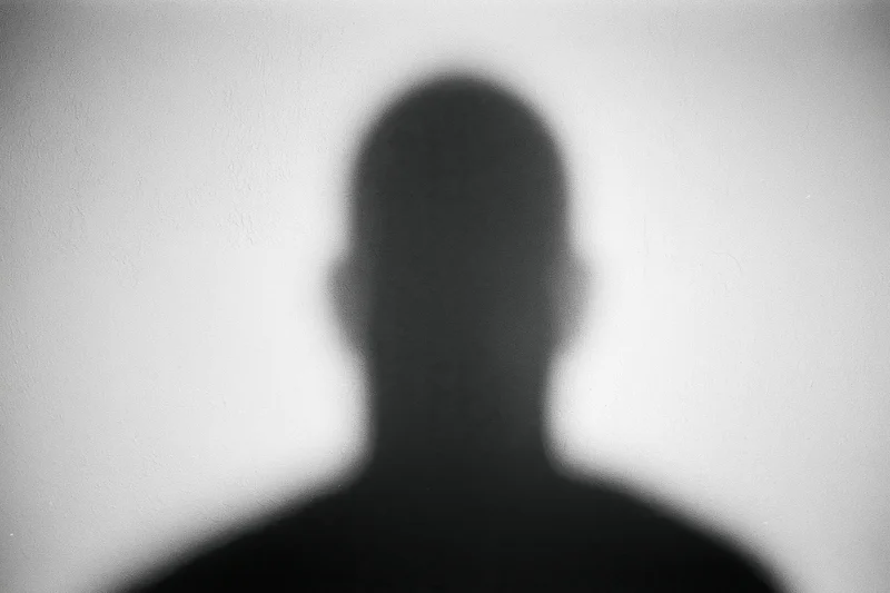 Blurred silhouette of a person's head and shoulders cast on a white wall