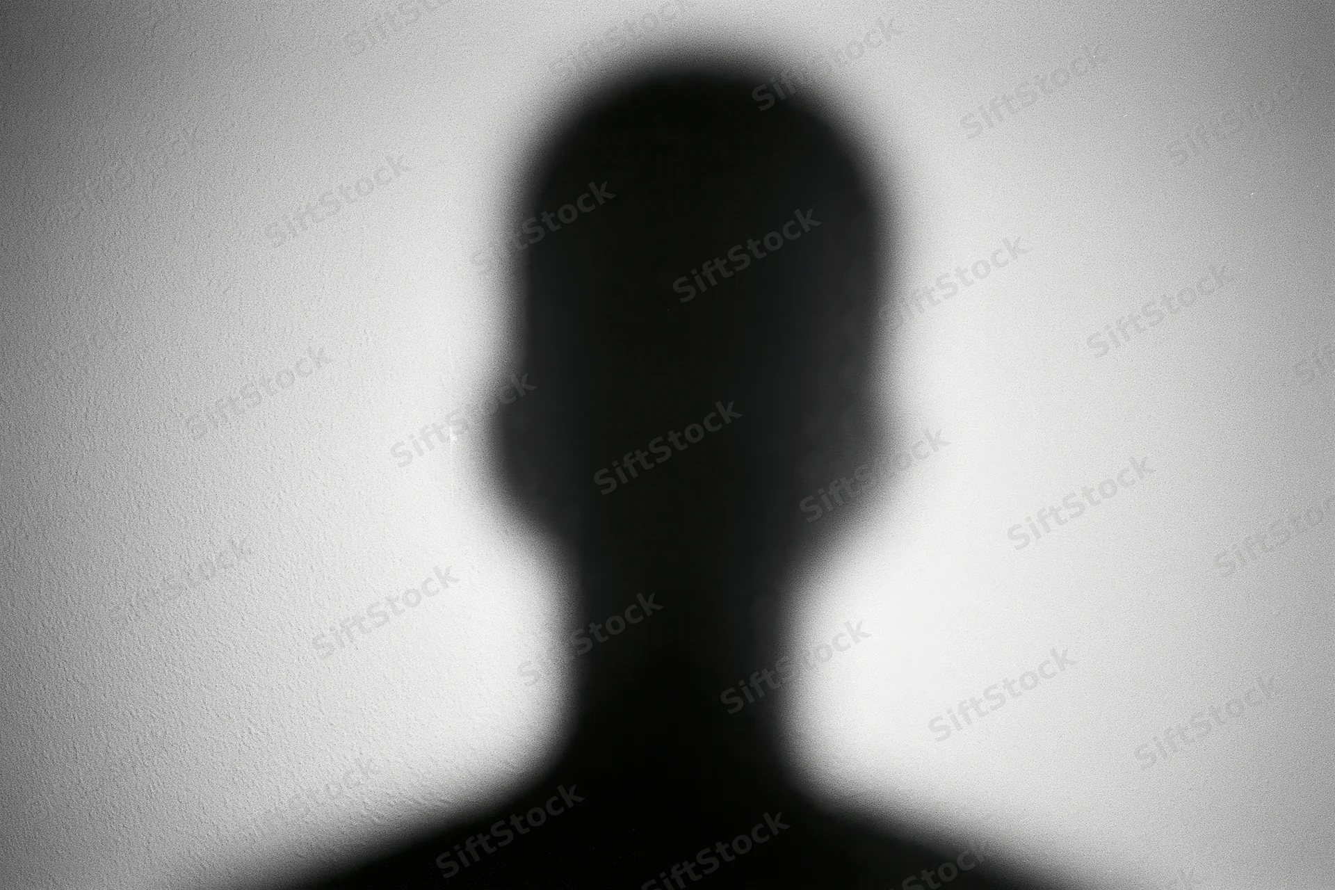 Blurred silhouette of a person's head and shoulders projected on a white wall
