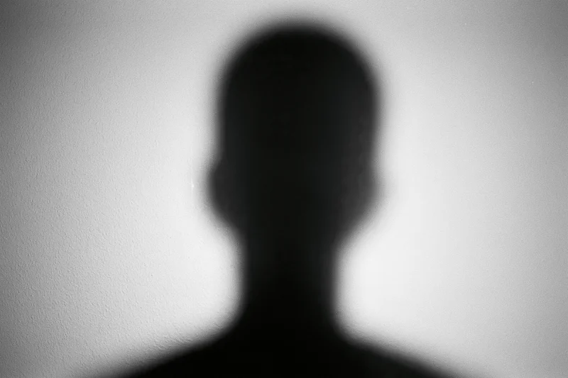 Blurred silhouette of a person's head and shoulders projected on a white wall