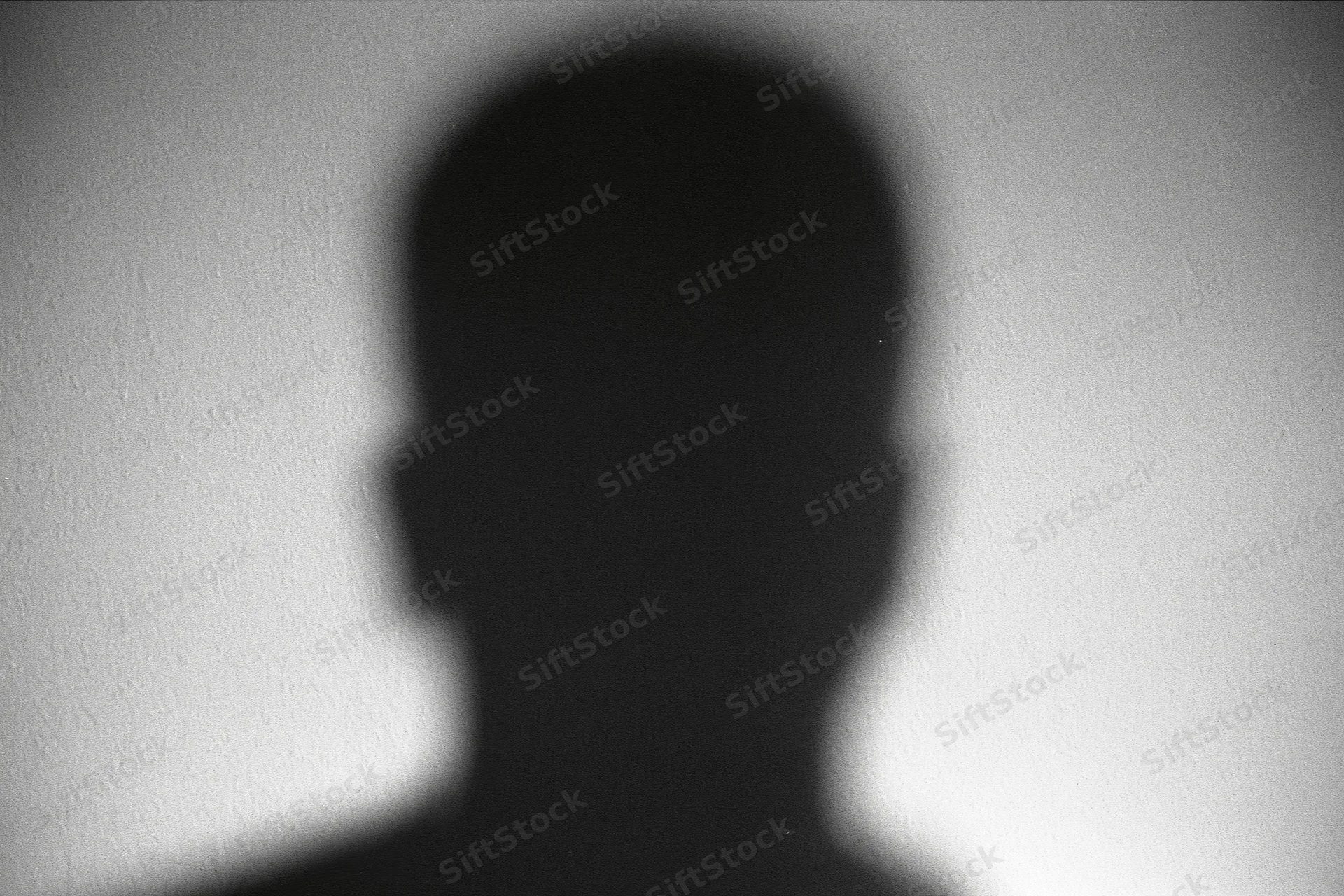 Blurred silhouette of a person's head and shoulders projected on a textured wall