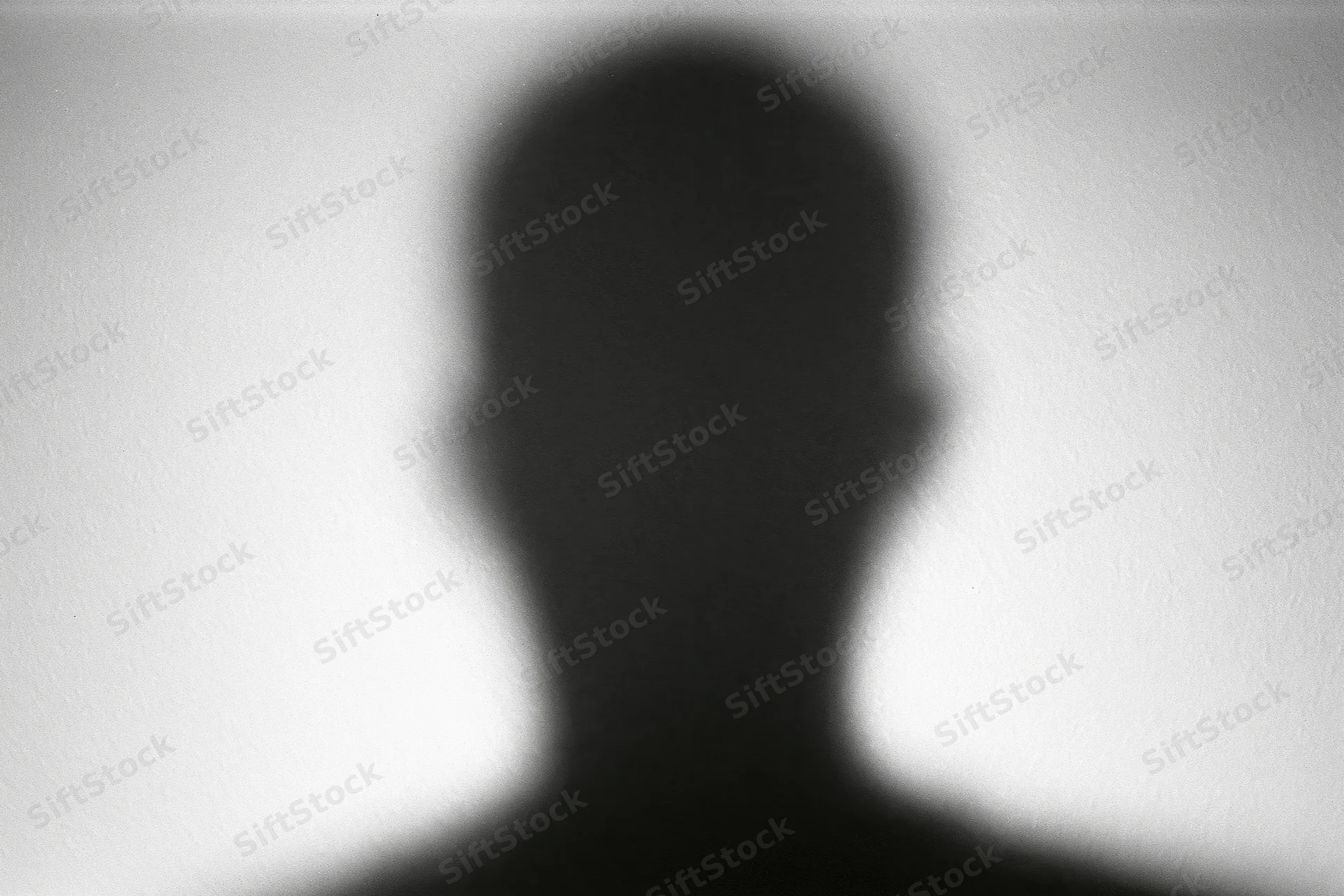 Blurred silhouette of a person's head and shoulders cast on a light wall