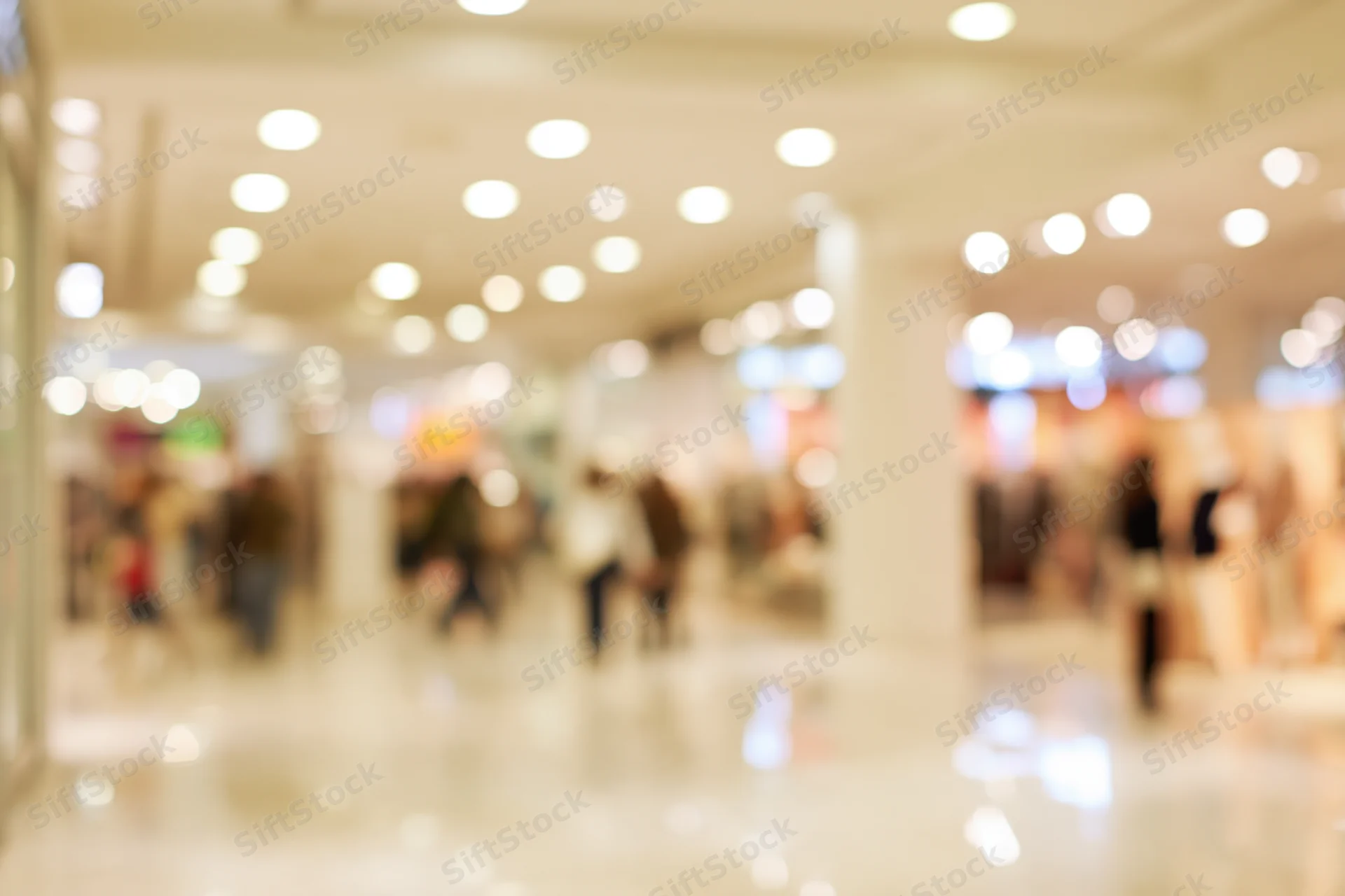Blurred interior of a busy shopping mall corridor with bokeh lights and moving people