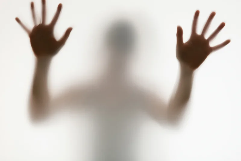 Blurred silhouette of a person pressing hands flat against frosted glass