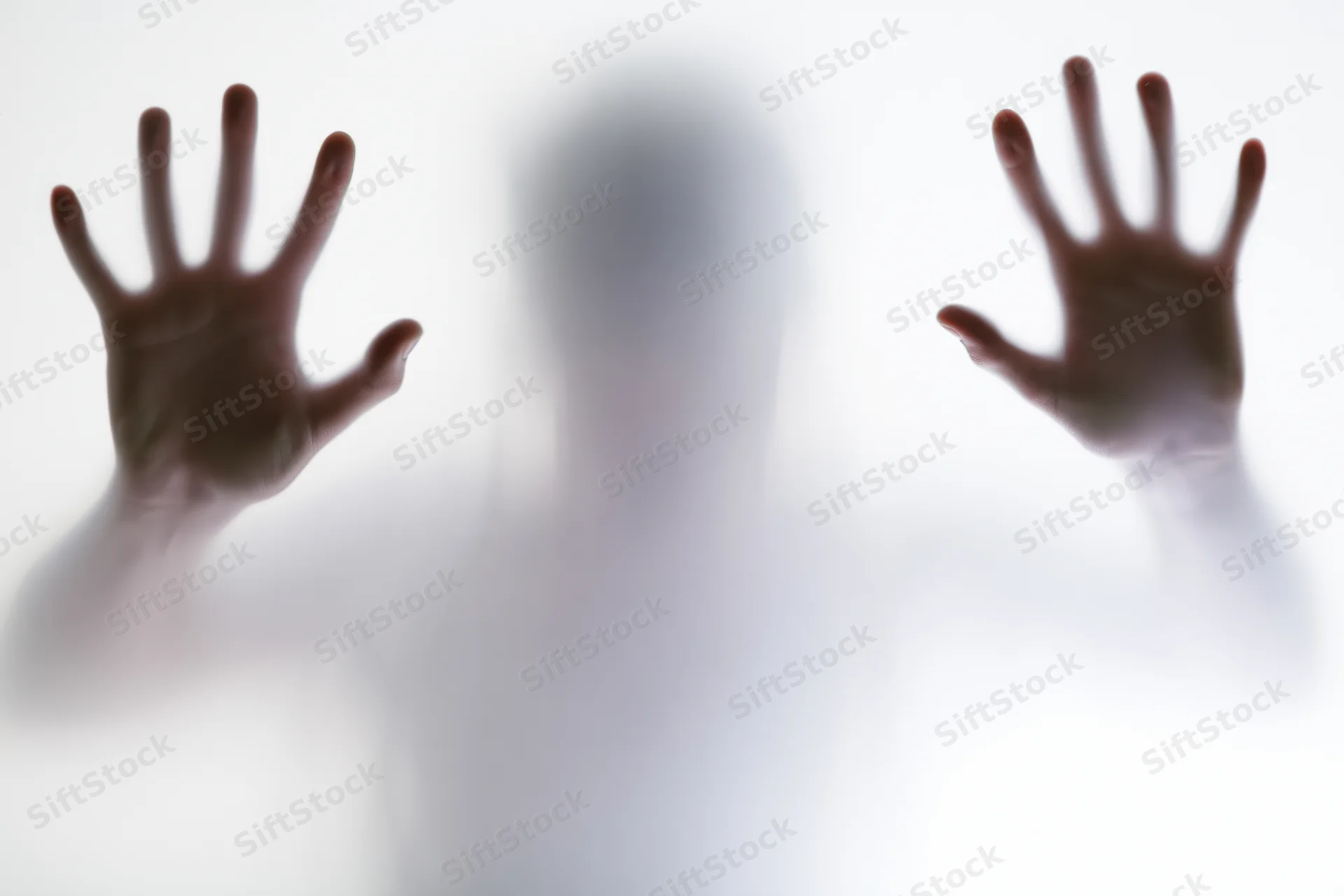 Blurred silhouette of a person pressing hands flat against frosted glass