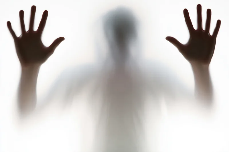 Blurred silhouette of a person pressing hands flat against frosted glass