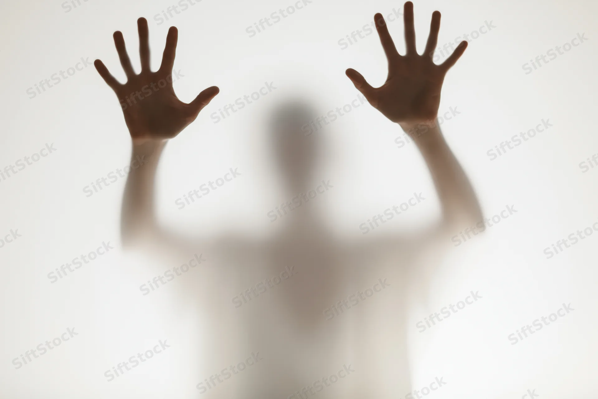 Blurred silhouette of a person pressing hands flat against frosted glass in a bright studio setting