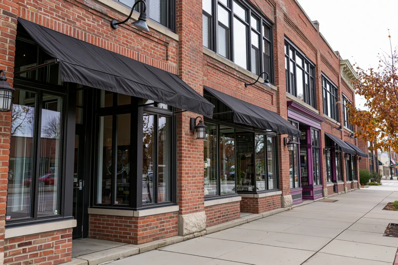 Row of brick storefronts with black awnings along an urban sidewalk