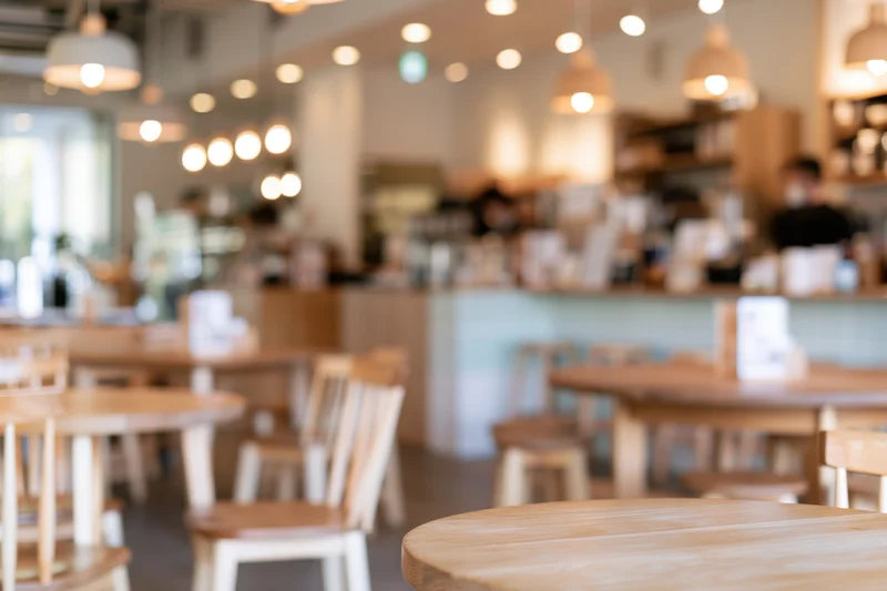 Wooden tables and chairs arranged in a bright modern cafe interior with pendant lighting and a blurred background