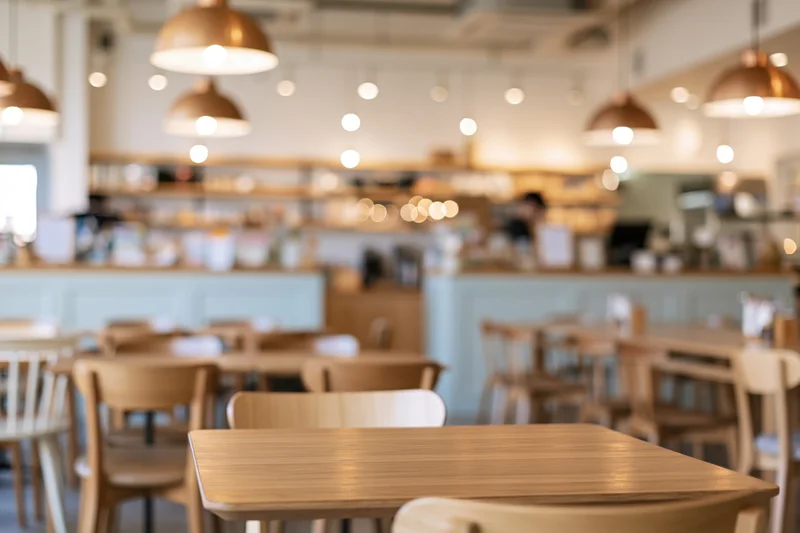 Wooden tables and chairs arranged in a modern cafe interior with warm pendant lighting and blurred background