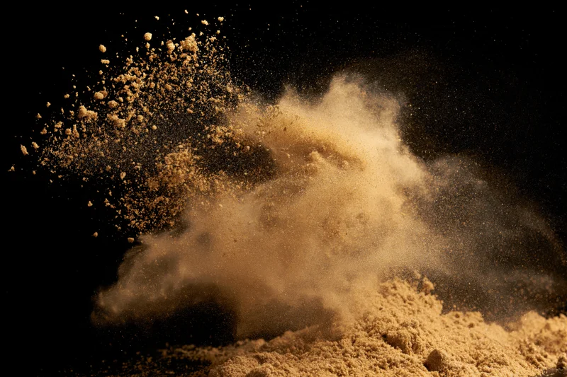 Golden-brown sand bursting into airborne particles against black background