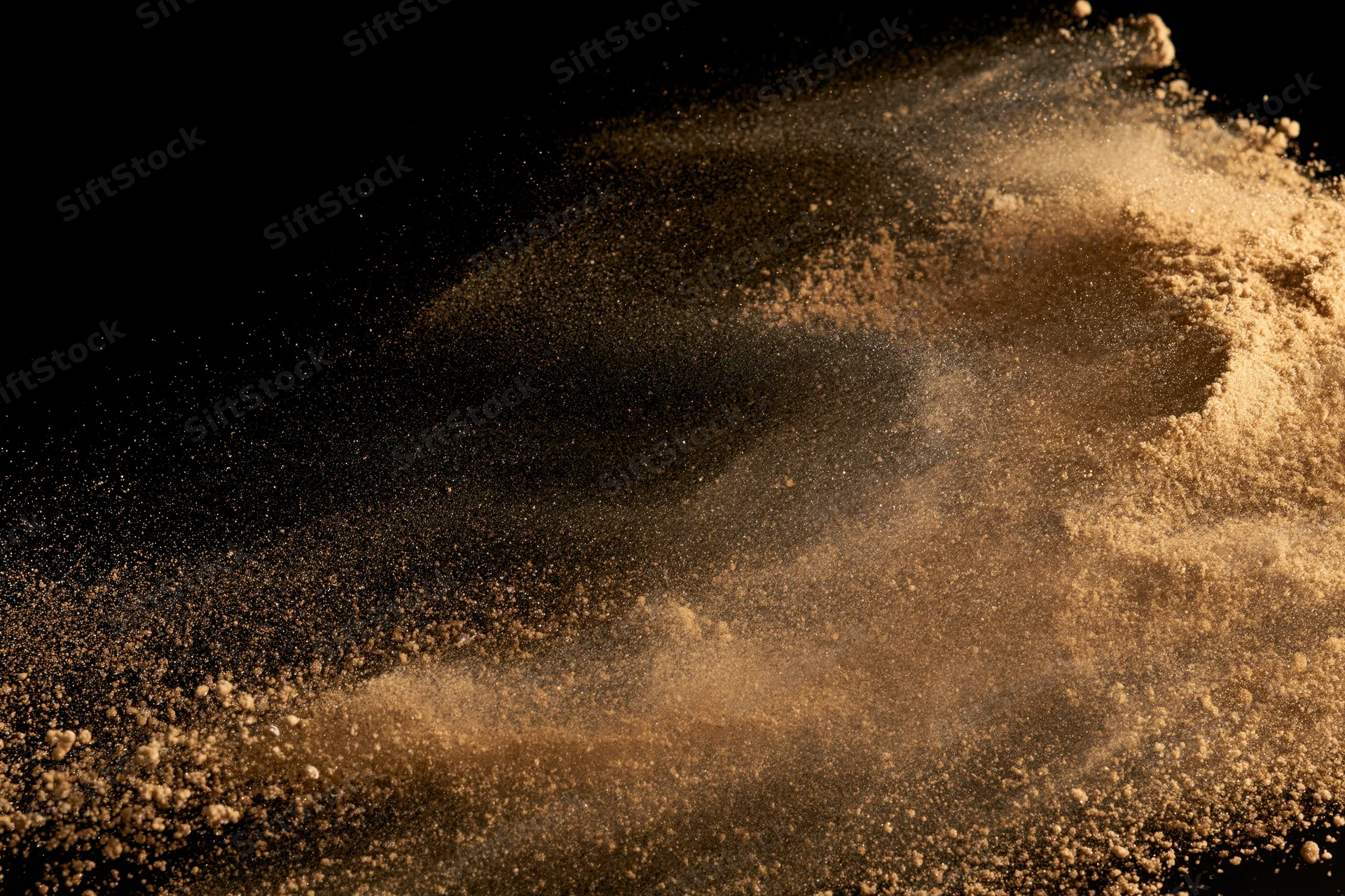 Golden-brown sand bursting mid-air in dynamic explosion against black background