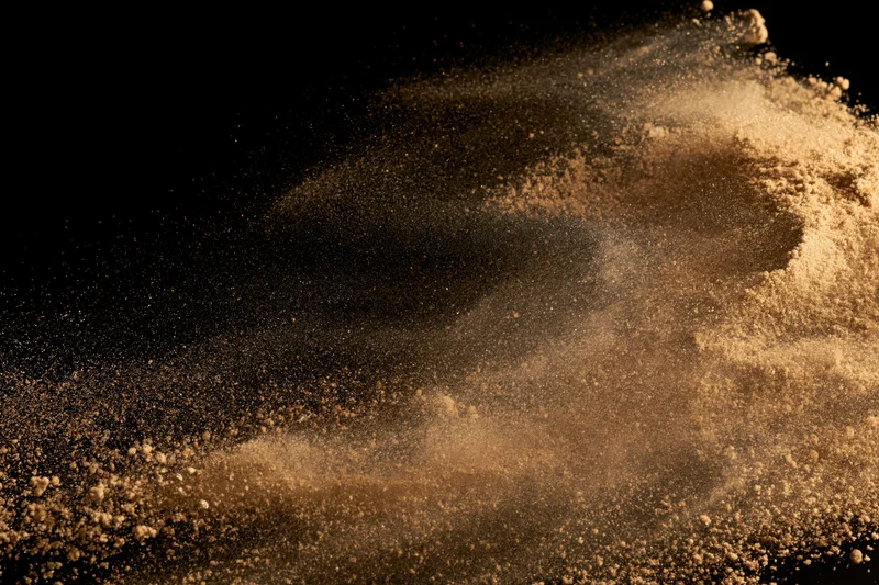 Golden-brown sand bursting mid-air in dynamic explosion against black background