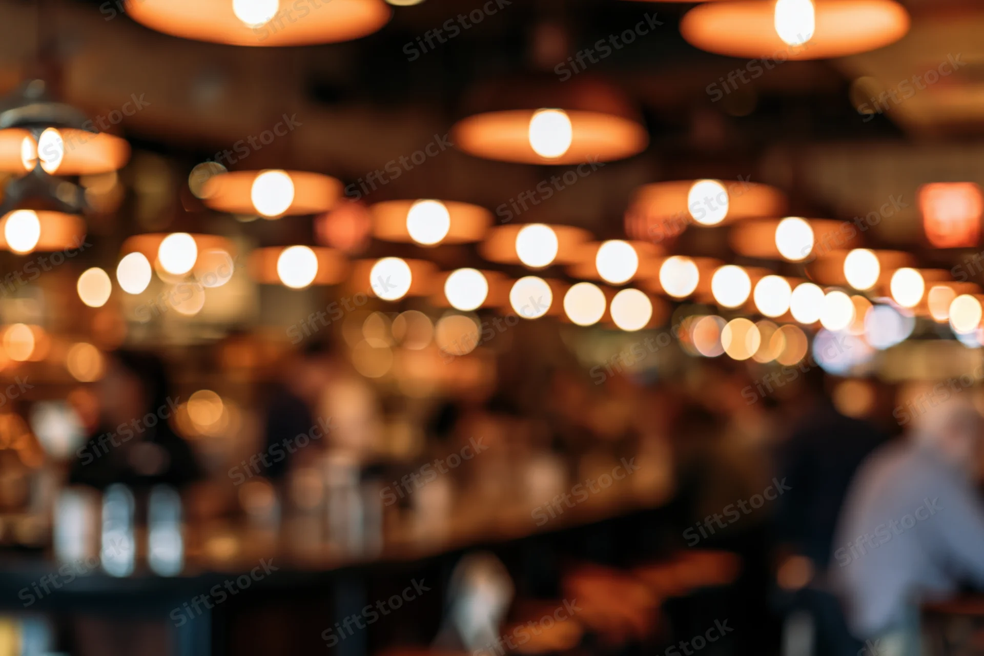 Blurred interior of a restaurant with warm pendant lights hanging from the ceiling