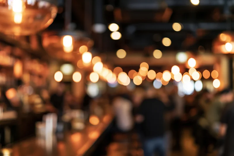 Blurred interior of a busy restaurant with warm pendant lights and people gathered around the bar