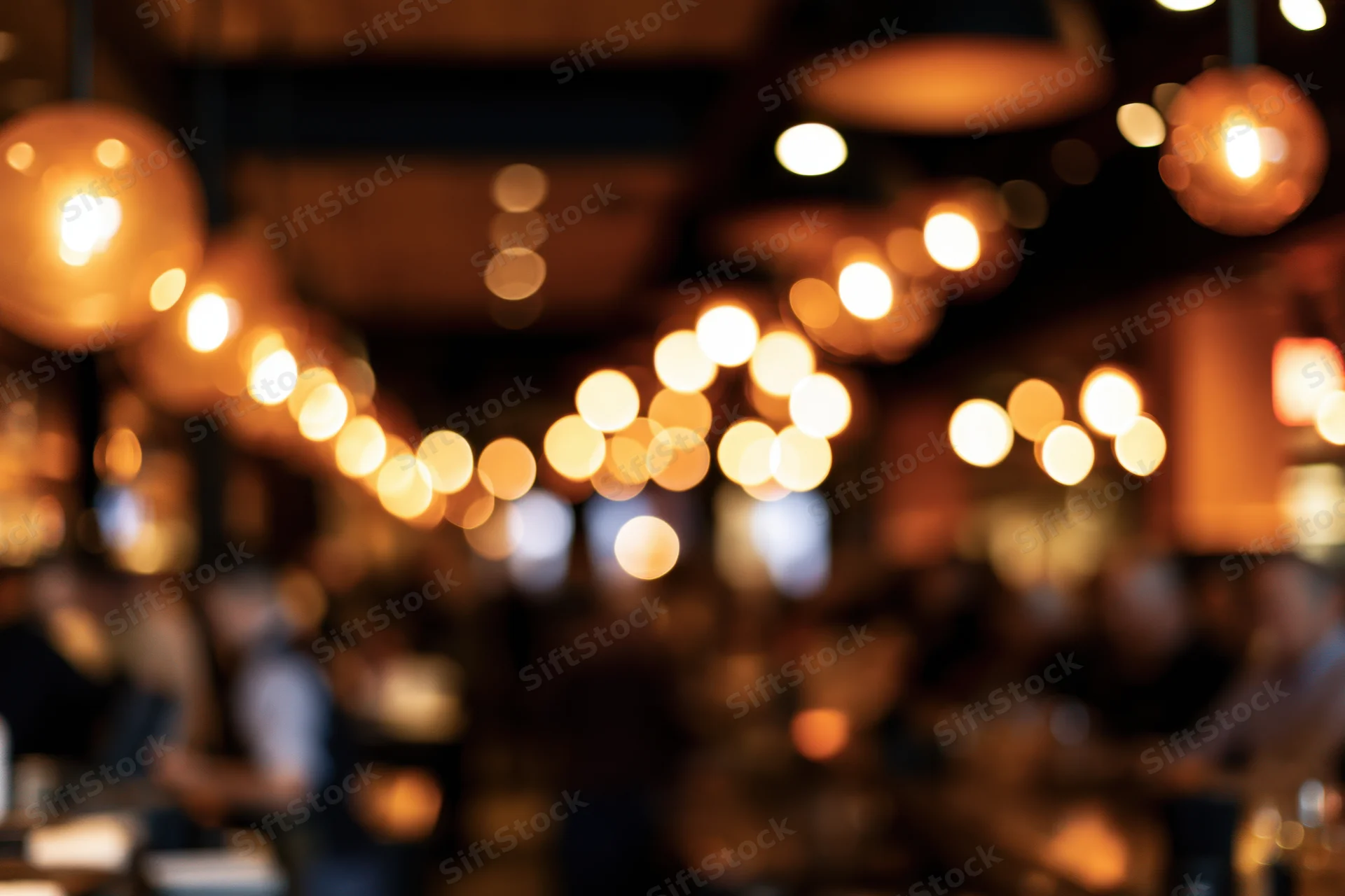 Warm pendant lights glowing softly in a blurred restaurant interior with seated people
