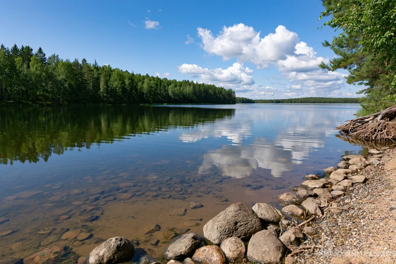 Calm inland lake with rocky shoreline and forest reflection under blue sky
