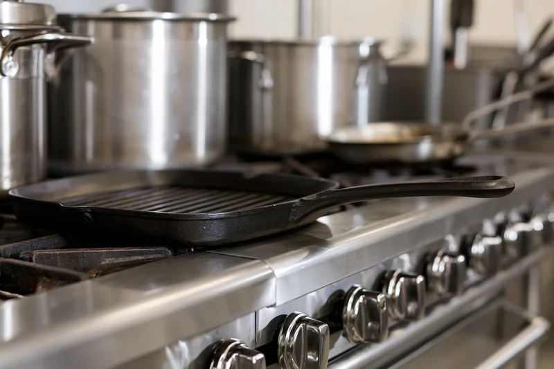 Cast iron grill pan resting on a professional stainless steel stove in a commercial kitchen