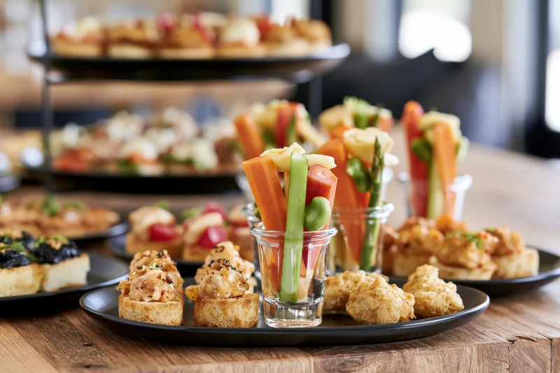 Assorted canapes and vegetable skewers arranged on black plates and glass cups on a wooden table