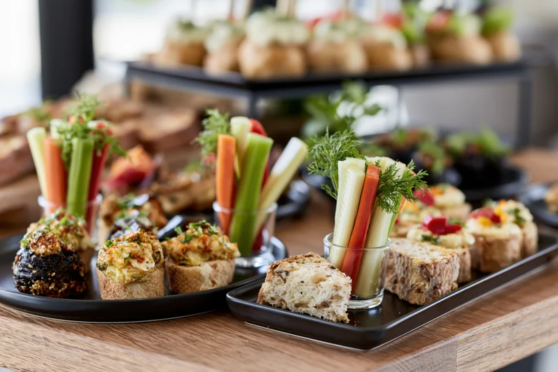 Assorted canapes and vegetable sticks arranged on black trays on a wooden table