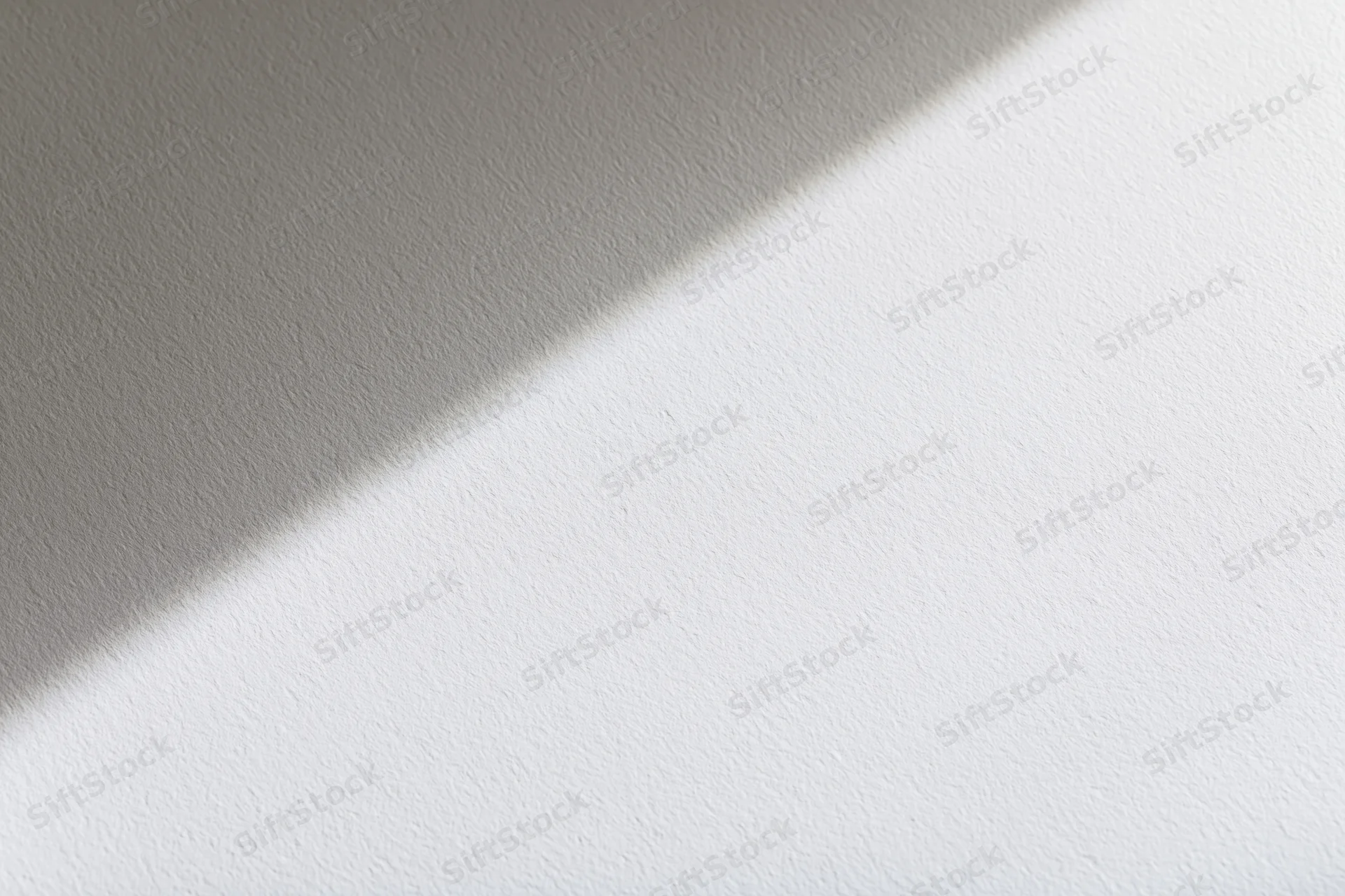 Diagonal shadow across a white textured surface in soft light