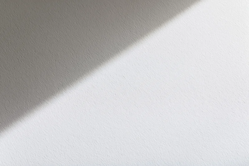 Diagonal shadow across a white textured surface in soft light