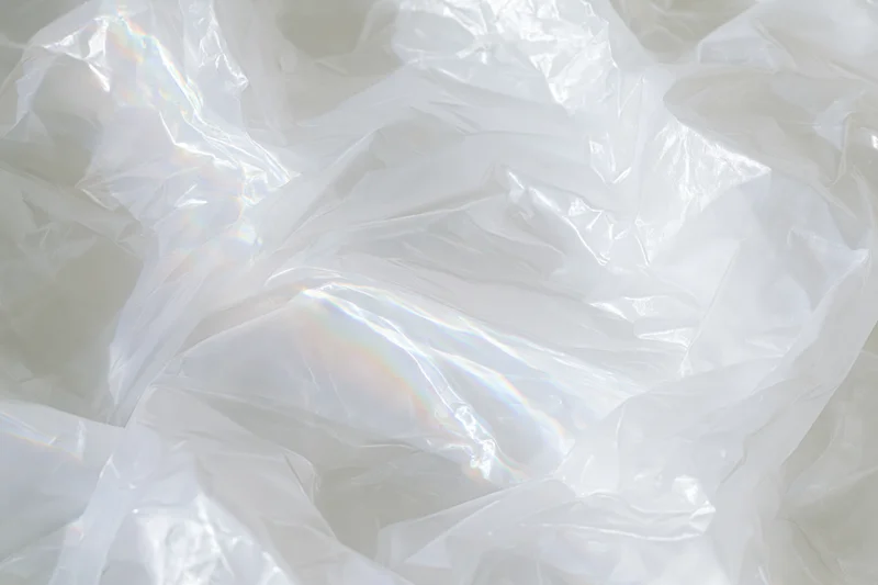 Crumpled translucent white plastic sheet with iridescent sheen and folds forming a textured surface