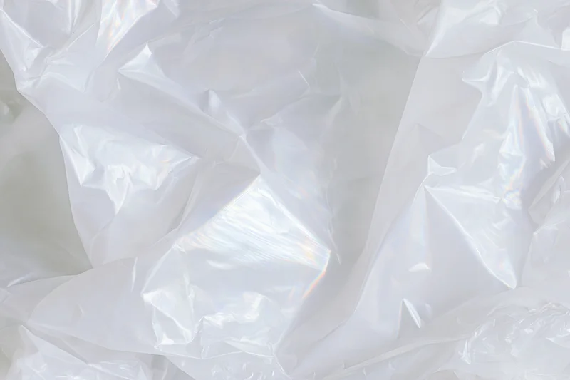 Crumpled white translucent plastic sheet with glossy folds and iridescent highlights filling the frame