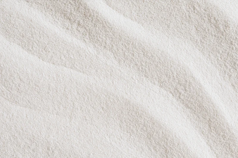 Close-up of fine white sand with smooth raked wave patterns in a flat lay arrangement