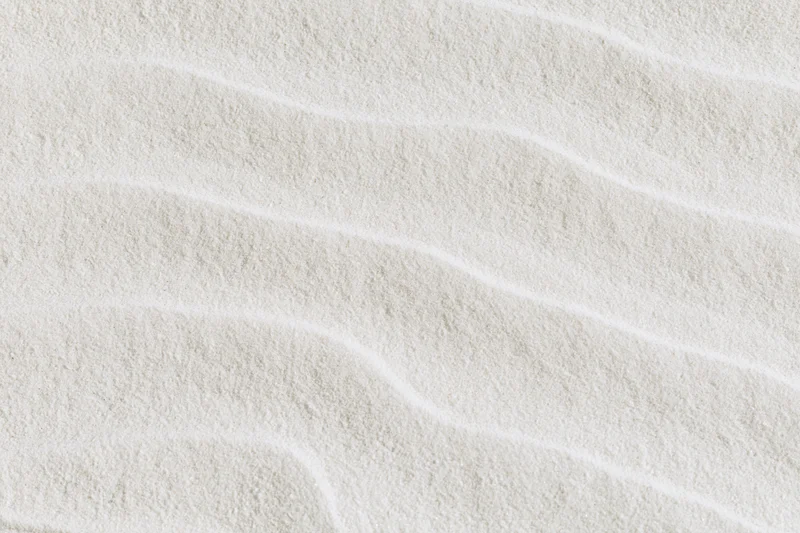 Close-up of fine white sand with smooth raked wave patterns in a flat lay arrangement