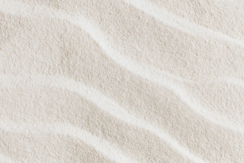 Close-up of raked white sand forming smooth wave patterns in a flat lay arrangement