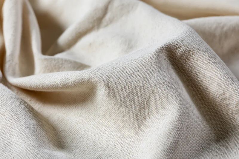 Close-up of natural unbleached cotton canvas fabric with soft folds and visible weave texture