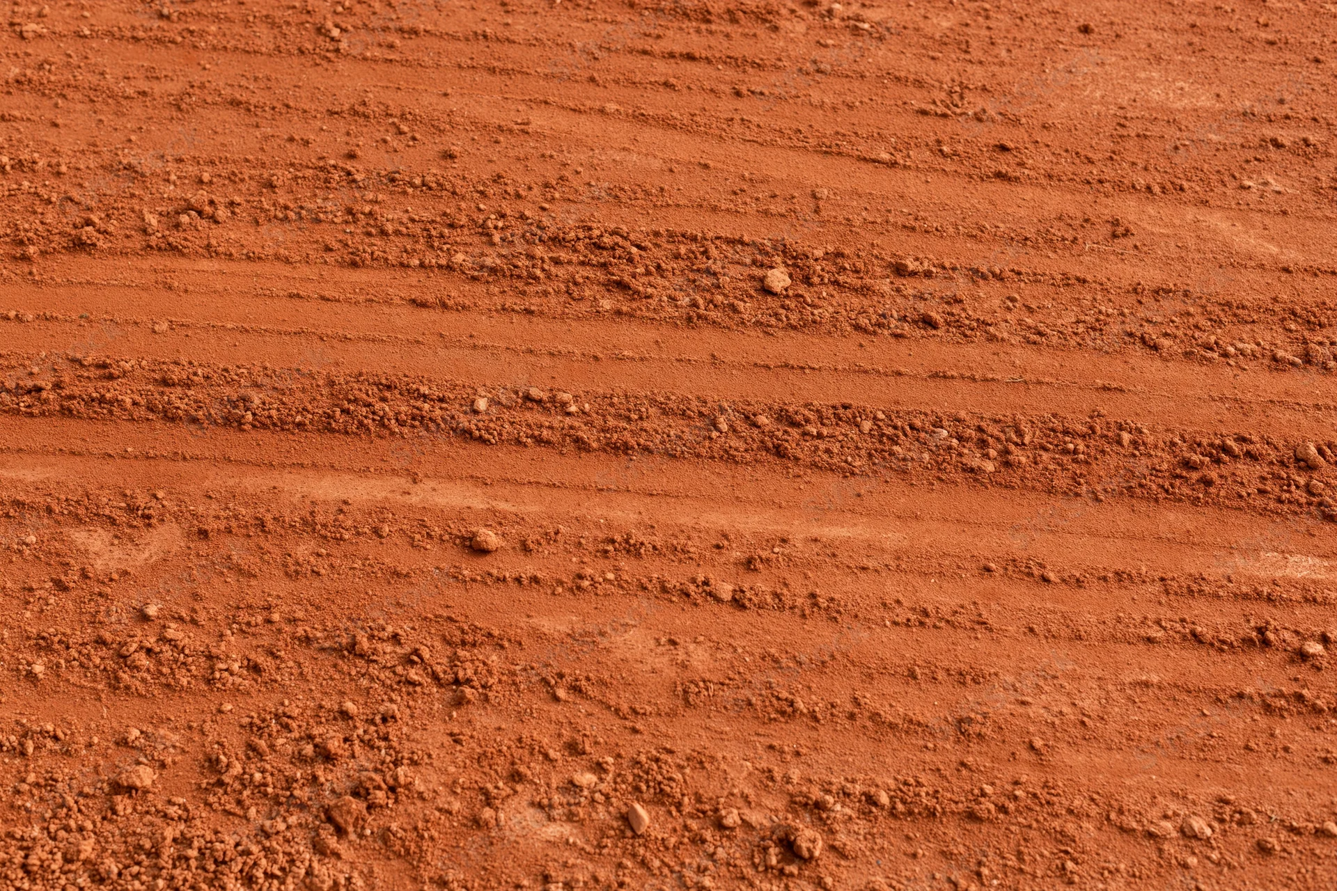 Close-up of rough red clay tennis court surface with horizontal grooves and texture