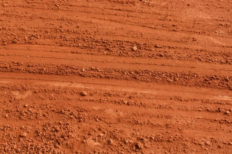 Close-up of rough red clay tennis court surface with horizontal grooves and texture