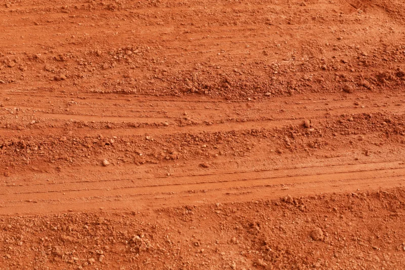 Close-up of rough red clay tennis court surface with tire tracks and soil texture