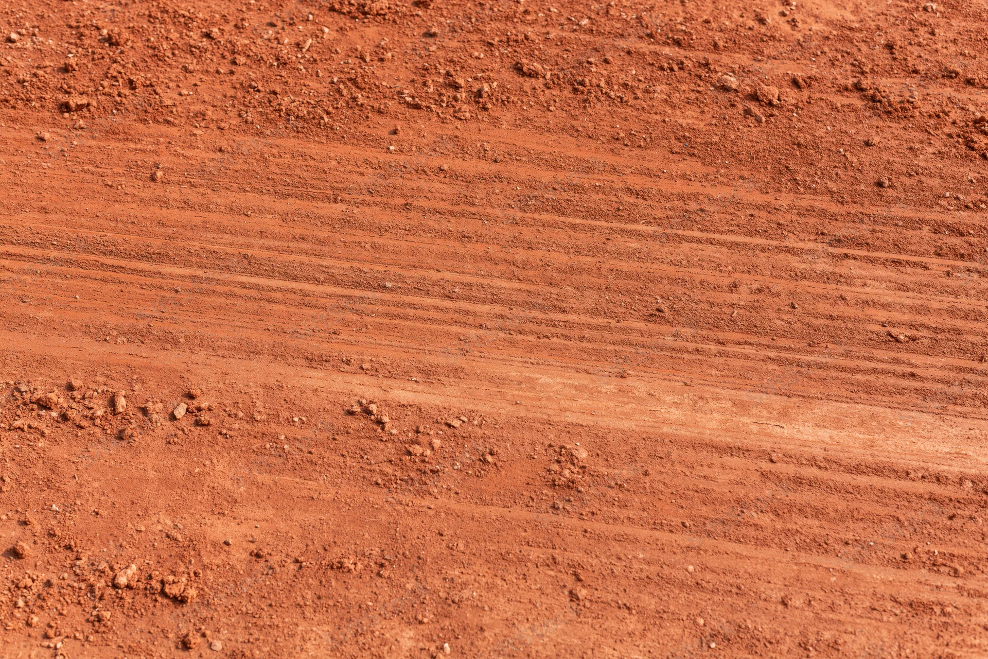 Close-up of rough red clay tennis court surface with visible tire tracks and soil texture