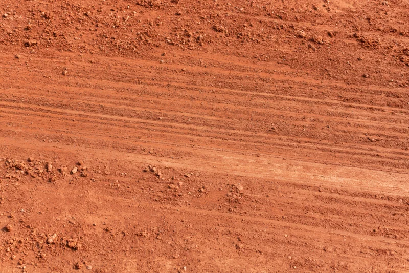 Close-up of rough red clay tennis court surface with visible tire tracks and soil texture