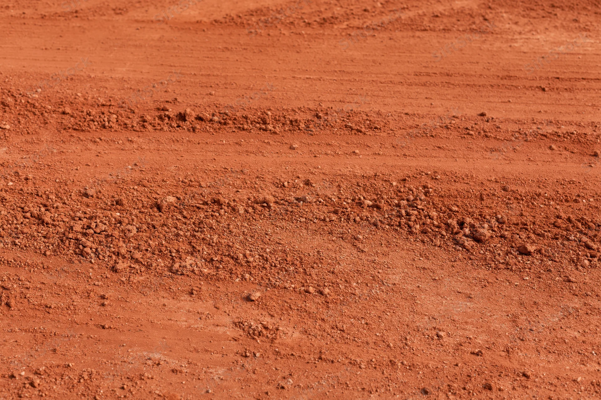 Close-up of rough red clay tennis court surface with visible texture and granular soil layers