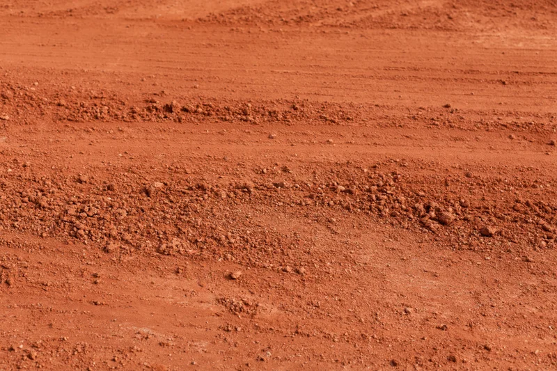 Close-up of rough red clay tennis court surface with visible texture and granular soil layers