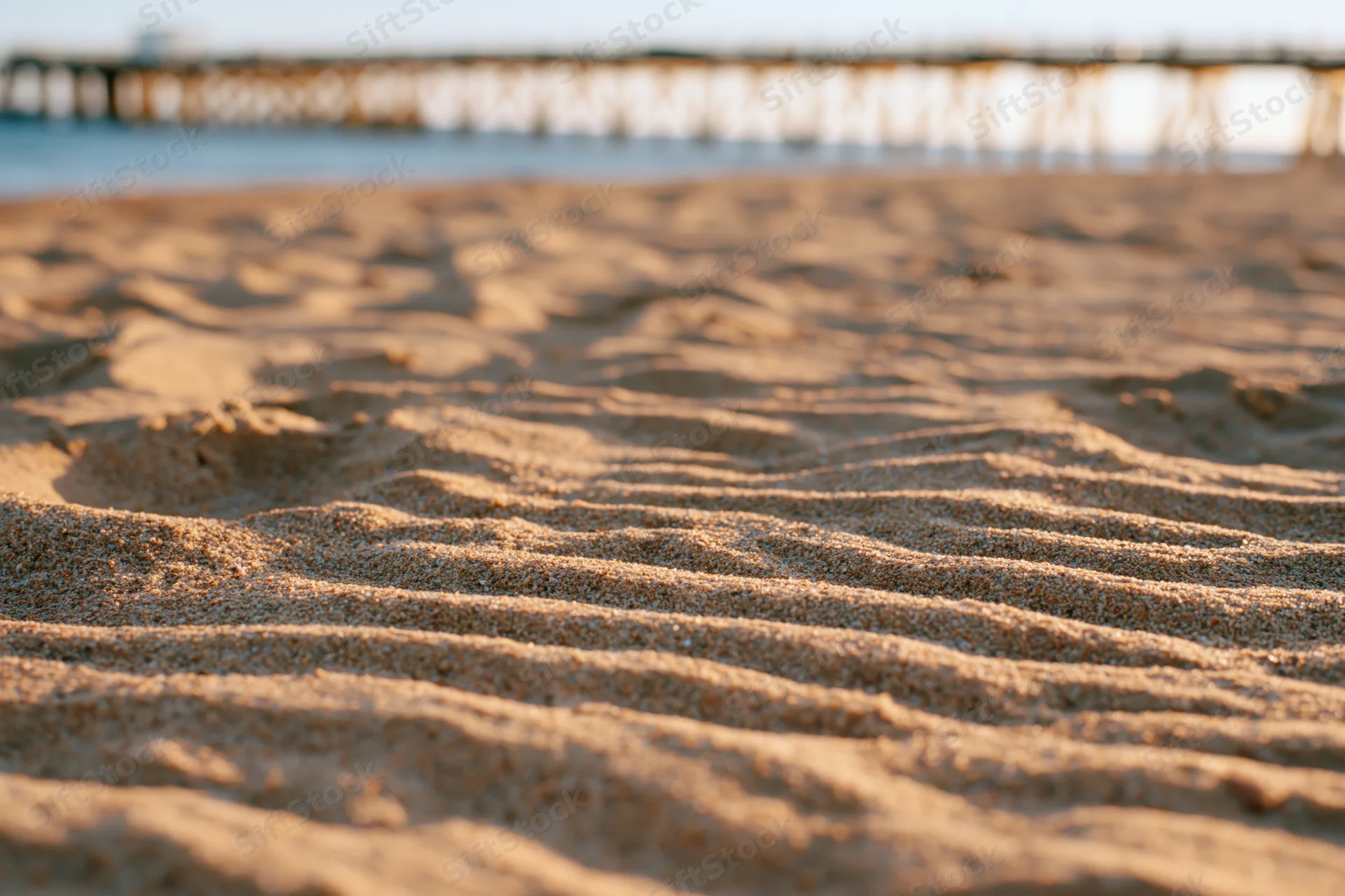 Rippled dry sand on a beach with a wooden pier in the background
