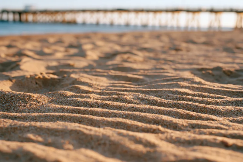 Rippled dry sand on a beach with a wooden pier in the background