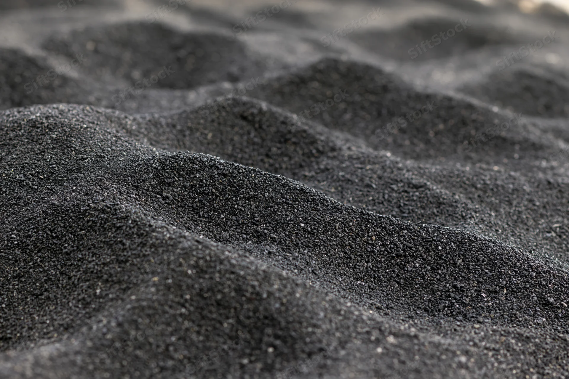 Close-up of black volcanic sand forming rippled patterns on a beach surface