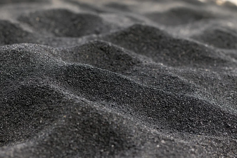 Close-up of black volcanic sand forming rippled patterns on a beach surface