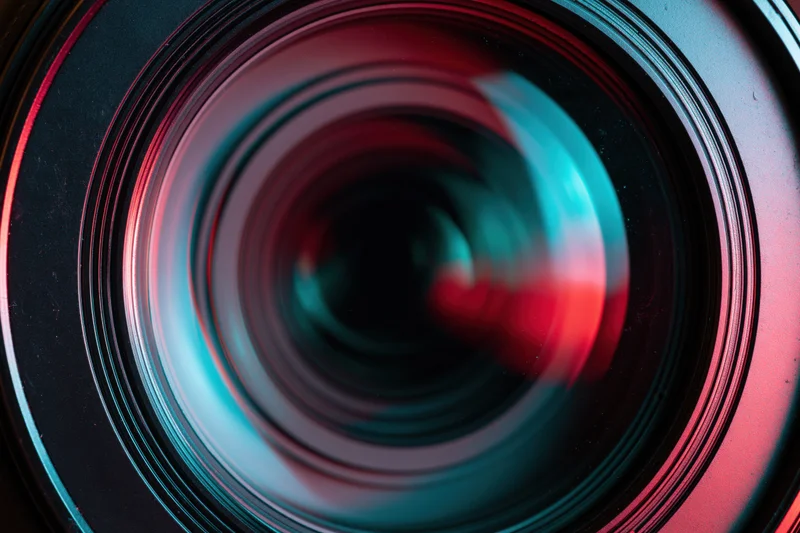 Close-up of a camera lens front element showing concentric glass rings with red and blue reflections