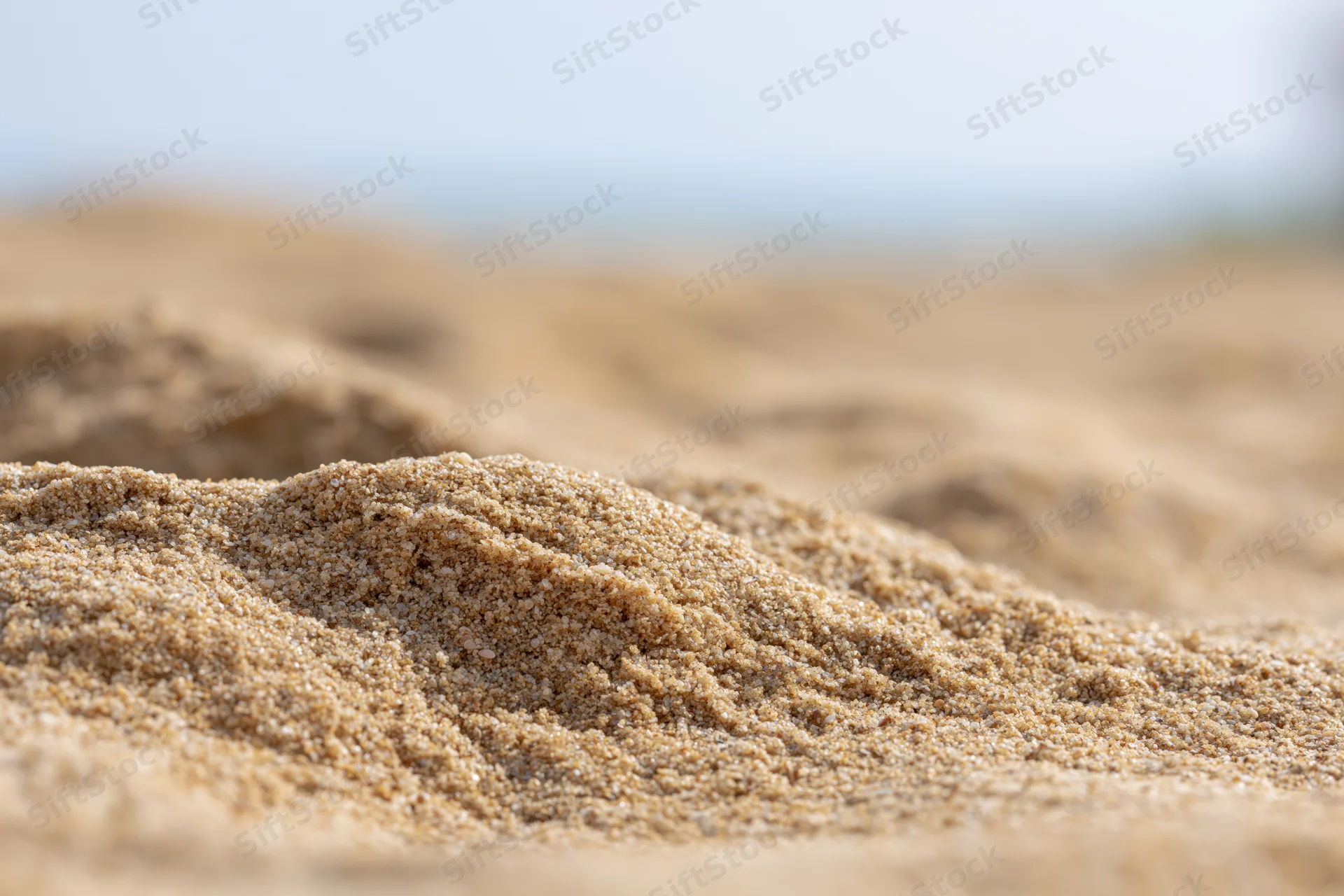 Close-up of dry beach sand mounded in the foreground with blurred background