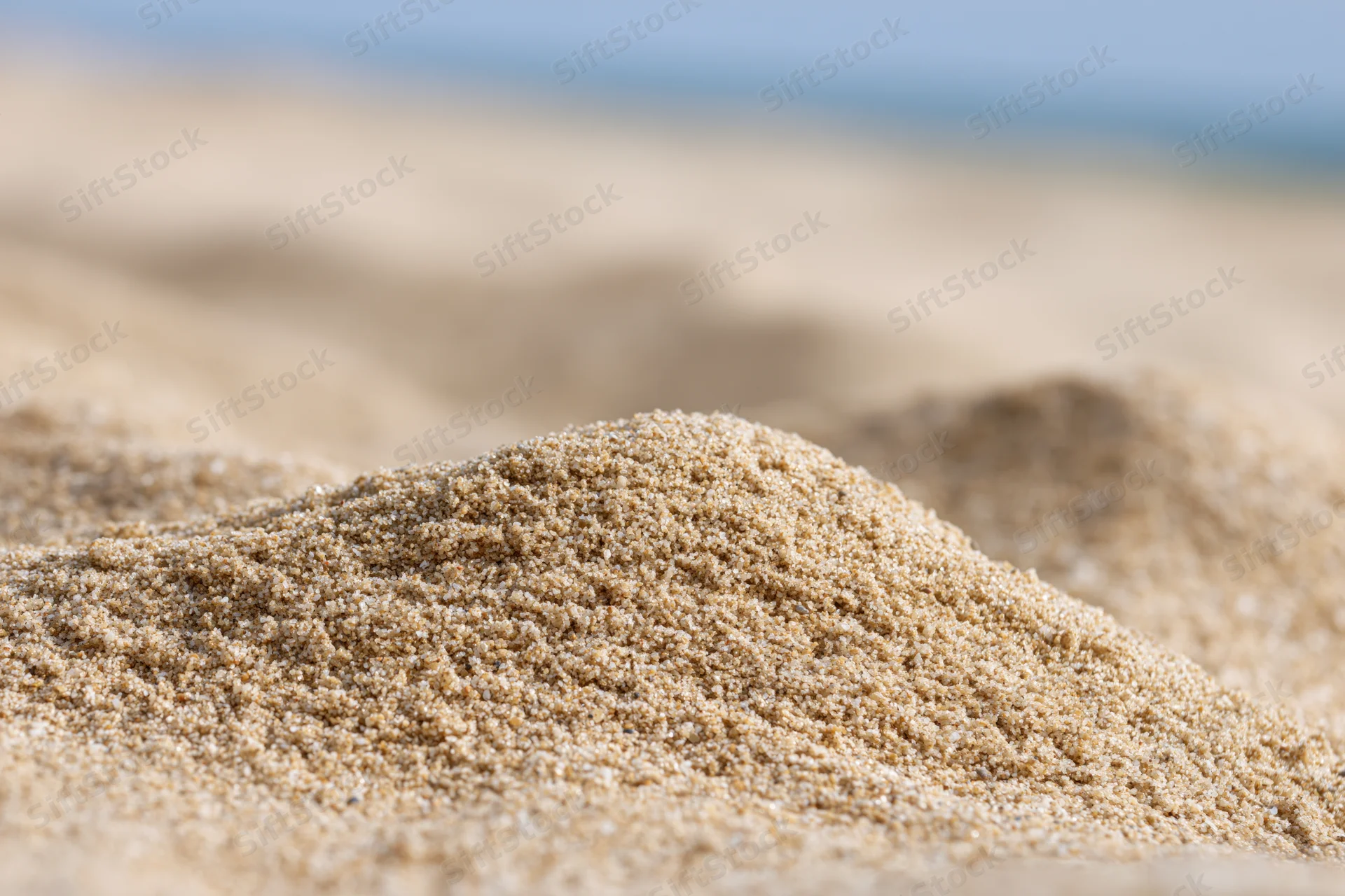 Close-up of mounded dry beach sand with blurred background under sunlight