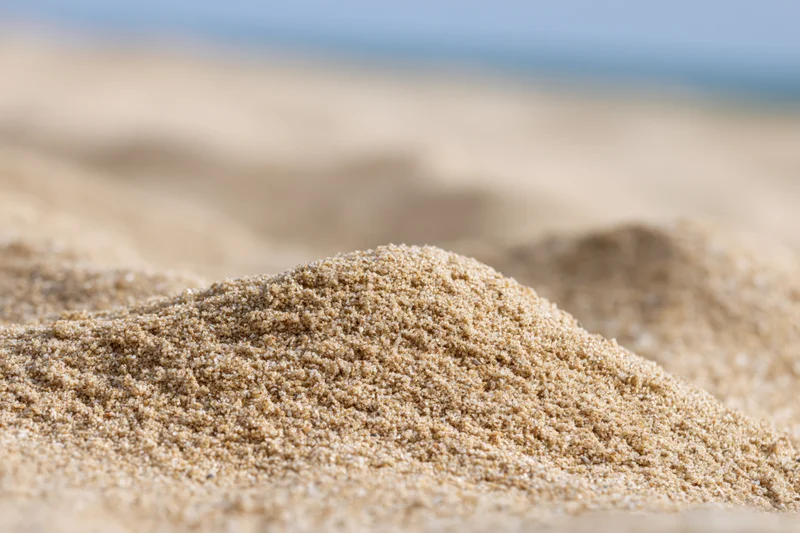 Close-up of mounded dry beach sand with blurred background under sunlight